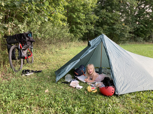 Dívka v lehkém stanu na louce vedle naložené bikepackingové kolo — malé dobrodružství s dcerou v přírodě